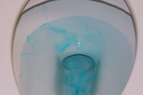 Toilet bowl showing colored water indicating a leak from the tank